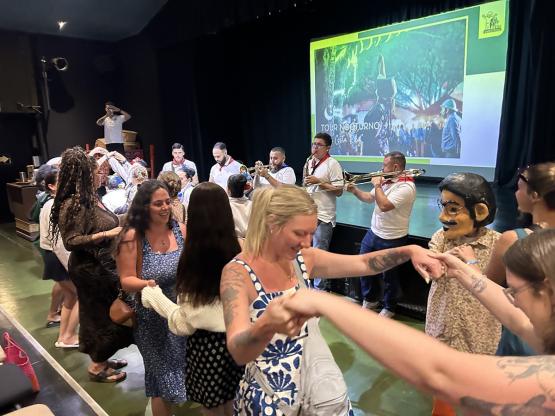 Individuals dance together while music  plays and one person wears a costume