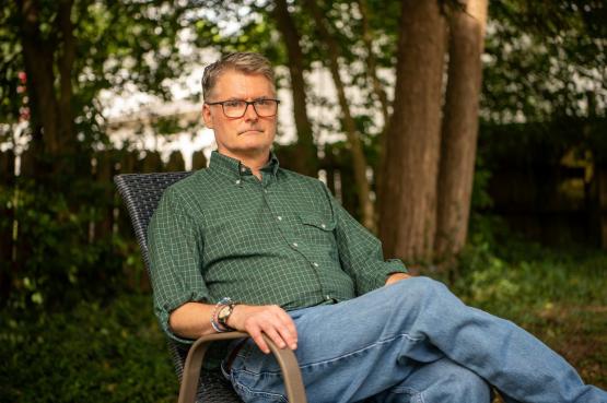 A man in a green shirt sitting down in a chair outside.