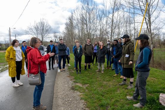 An OHIO faculty member talks to a group of students while standing outside on a paved bike path or small road, while some students stand in the grass