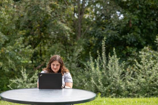 An OHIO student works on a computer while sitting at a table outside