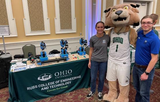 Brandon Petrie stands next to Rufus the mascot and another OHIO student and next to a Russ College of Engineering and Technology booth 