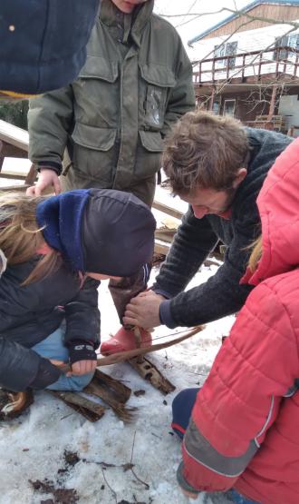 Joe Brehm leans in the snow with other individuals while he holds a tool and works on a project