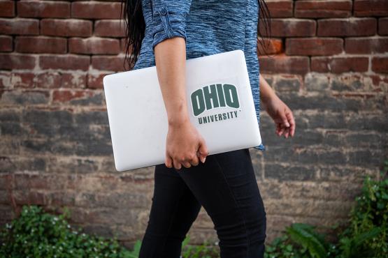An OHIO Online student walks with a laptop with the Ohio University logo on it.