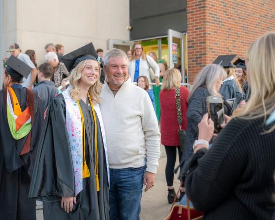 A family member poses with a graduate while other people stand nearby after the Graduation Recognition Ceremony at Ohio University Lancaster