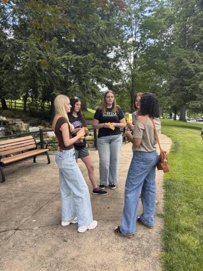 5 female students standing outdoors in a park, in a circle talking to each other