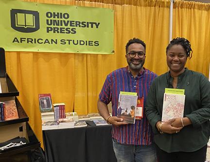 Jody Benjamin and Ademide Adelusi-Adeluyi hold their books and stand by a banner that says "Ohio University Press - African Studies"