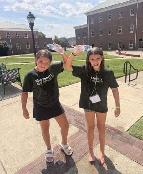 Two students in the Bobcat Academy pour water on their heads while standing outside on a warm summer day at Ohio University Southern