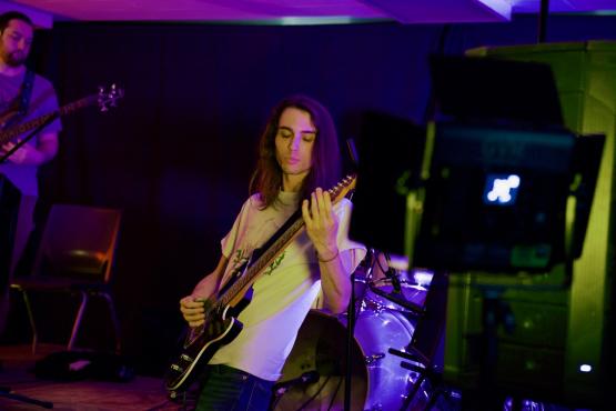 An individual plays guitar while another person plays a guitar in the background