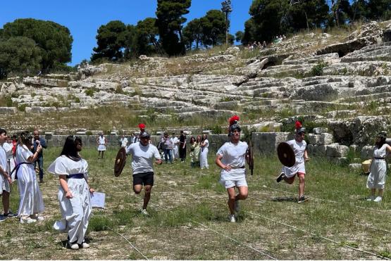 People in traditional Greek helmets with feathered plumes race through a field