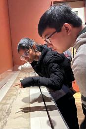 Two students lean over a glass-enclosed Chinese scroll in a museum