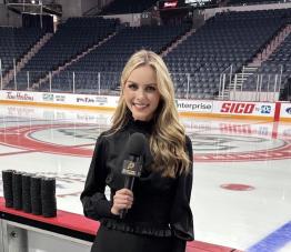 Hailey Hunter stands rinkside at the Pittsburgh Penguins arena, holding a microphone