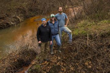John Sabraw, Michelle Shively, and Guy Riefler pose with a creek behind them.