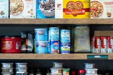 A photo of food pantry shelves filled with cereals, canned good, baking items, spices, coffee and other items