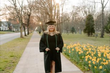 Graduate in cap and gown walking next to daffodils