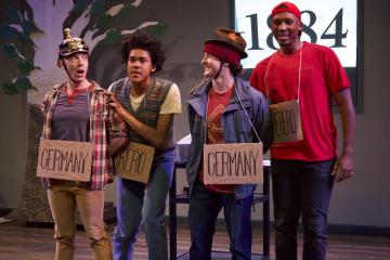 Four actors stand side-by-side with cardboard signs strung around their necks
