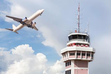 A plane flies next to an air traffic control tower.