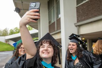 Nikki Wood and other OHIO graduates take a selfie while wearing Commencement caps and robes and standing next to the Convocation Center.