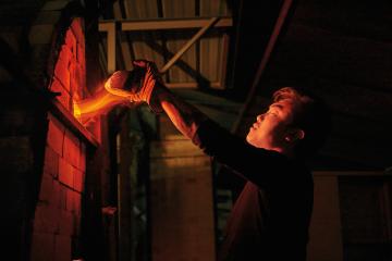 flames shoot from a small gap as a graduate student wearing gloves removes a brick from a kiln to check on its contents