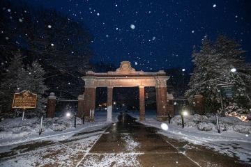 Snow falls on Alumni Gateway at night
