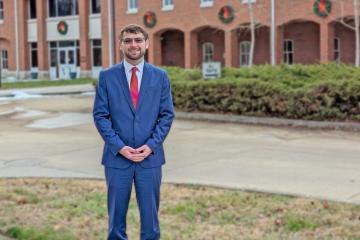 Man in suit stands in front of brick building