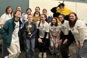 Participants and organizers from a spelling bee competition at Ohio University stand together for a photo. One person is wearing a bee costume.