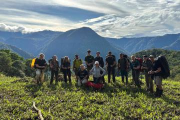 A group of hikers standing atop a forested hillscape.