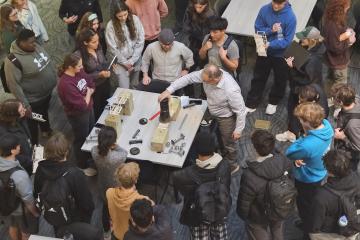 A Learning Community instructor works on a project at a table while a large crowd of students watches