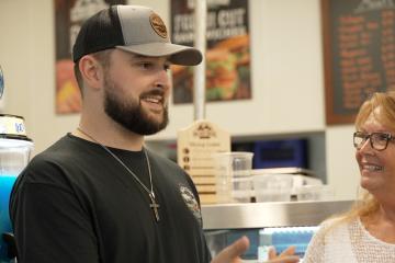 An individual from the High Street Deli speaks to a representative from the Small Business Development Center