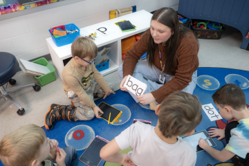teacher candidate works with children to read notecards on carpet