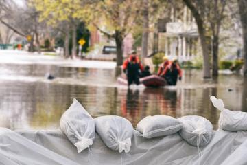 emergency workers wade through flood waters with sandbags in the foreground