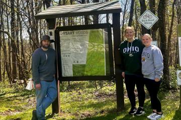 Photo of 3 people standing next to a sign at the entrance of Dysart Woods:  Marshall Dyer, Sophia Withrow, Kiara Triplett