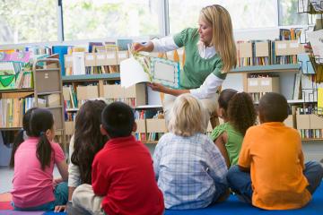 Children sit in a semi-circle around a teacher who is reading them a book
