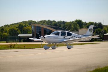 A plane with an OHIO logo on it is shown flying just above the aiport runway, and the Gordon K. Bush Airport is shown in the background
