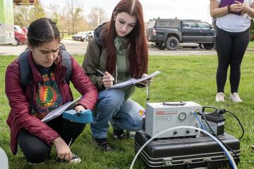 Two geology students study paperwork during a lab at Ohio University beside geology equipment set up on the ground.