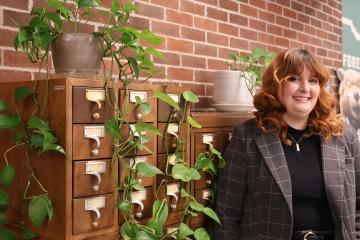 Haley Shaw stands next to a card catalog that hs plants on it, and there is a Forever OHIO banner on a wall in the background