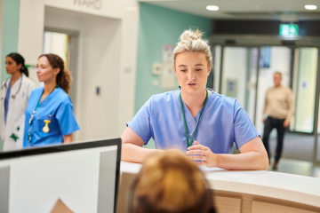 healthcare worker standing at desk talking to woman on computer