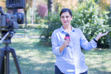 student reporter standing outside holding a microphone and facing the camera