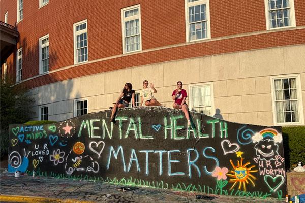 students sit on top of a wall with graffiti saying mental health matters