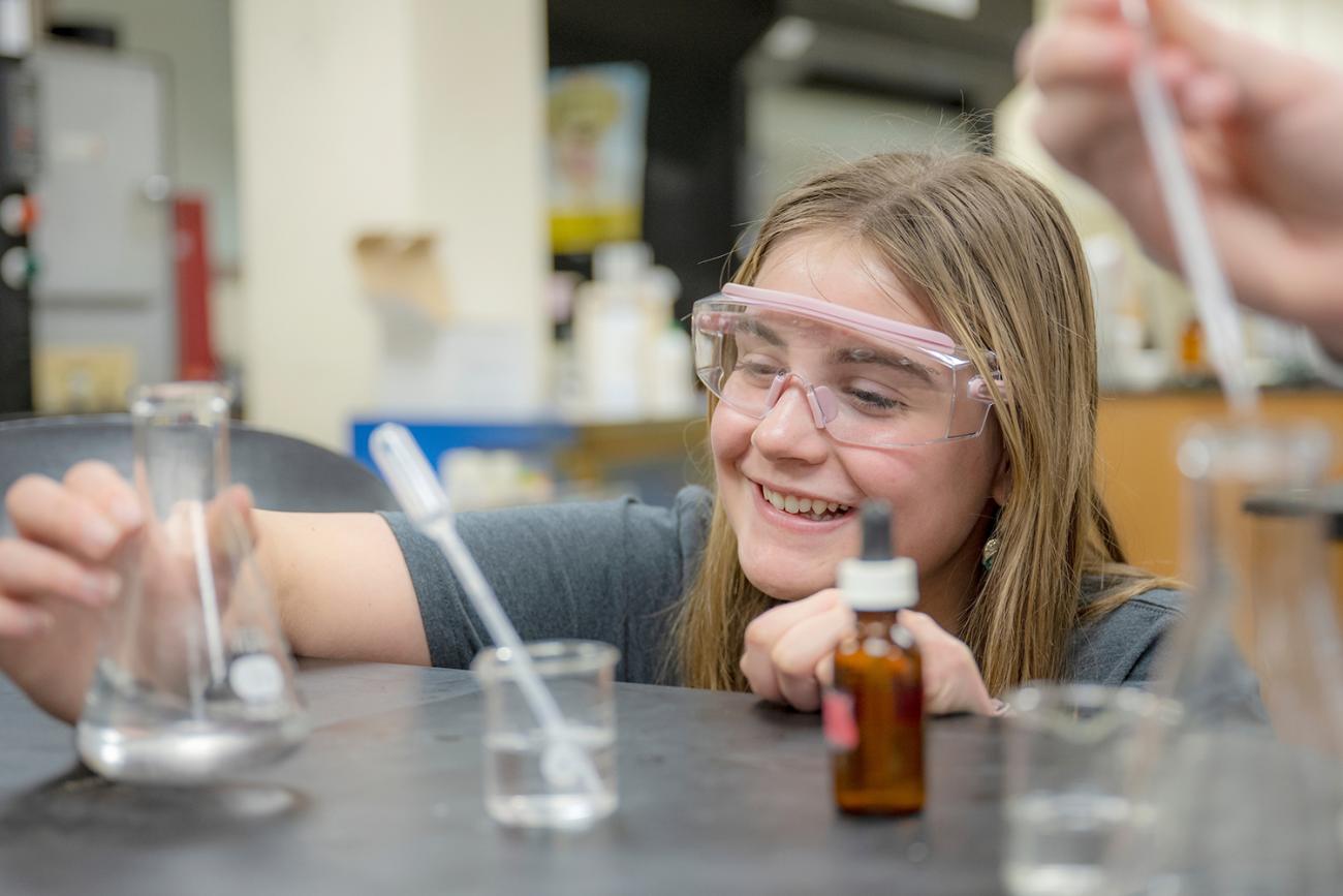 Woman in a science lab using a dropper to drop liquid into graduated cylinder 