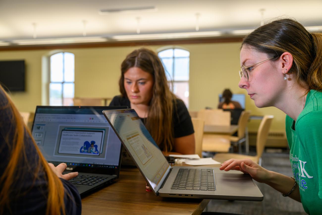 two women looking at laptops on a desk in a classroom