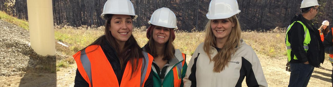 Three female students with hardhats under a freeway overpass