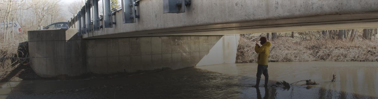 A road bridge over a creek with a person working beneath it