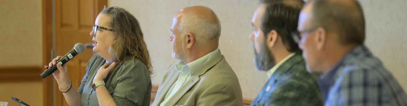 Panel members, one speaking into a microphone. 