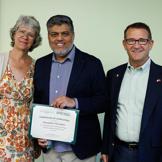 man receives certificate and stands between a man and woman
