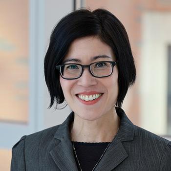 Lareina La Flair - Headshot, smiling woman with dark framed glasses, chin length black hair and dark suit 