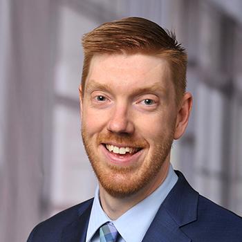 Robert Ashmead headshot, smiling man with short red hair in blue suit and tie
