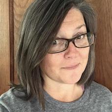 Headshot of Jenny Jones, woman with brown shoulder length hair, dark-framed glasses and a gray shirt. 