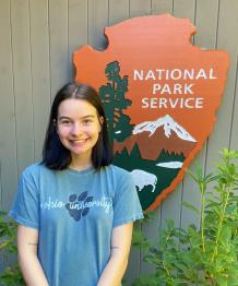 Smiling woman standing in front of a National Park Service Emblem in an outdoor space